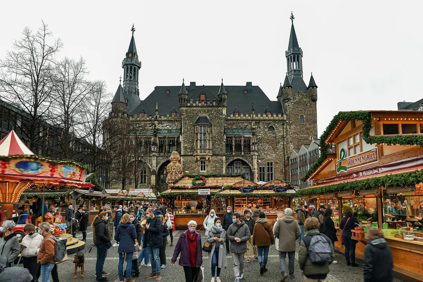 Bezoekers tussen de kramen op de Markt in Aken, met het stadhuis op de achtergrond