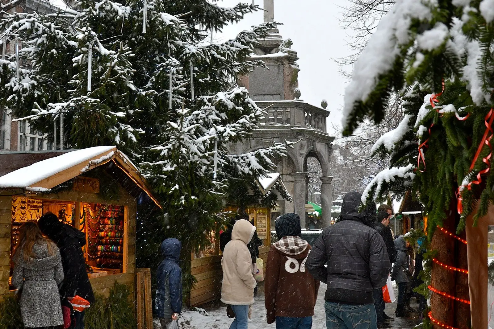 Bezoekers tussen besneeuwde chalets van het Village de Noël bij de Perron in Luik