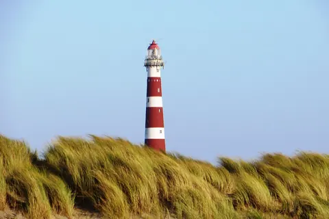 De rood-wit gestreepte vuurtoren Bornrif bij Hollum op Ameland, boven het helmgras van de duinen