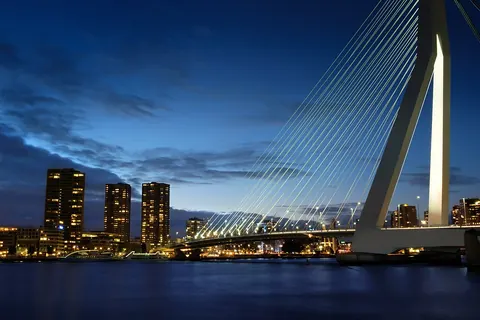 De verlichte Erasmusbrug en de skyline van Rotterdam in het blauwe uur